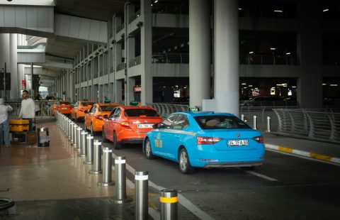 Vibrant taxis lined up at Istanbul Airport arrival terminal with passengers and drivers interacting.